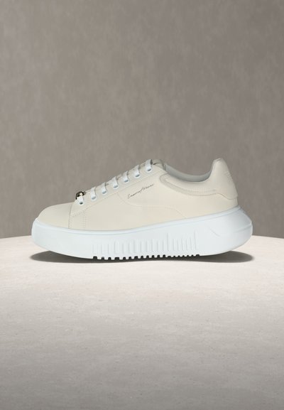 Λευκό sneaker χαμηλού τύπου με παχιά υφή στη σόλα, κλείσιμο με κορδόνια και διακριτικό λογότυπο της μάρκας στο πλάι, εμφανίζεται σε ουδέτερο φόντο.