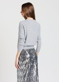 Grauer Strickpullover mit langen Ärmeln und geripptem Saum, kombiniert mit einem mit Pailletten verzierten silbernen Rock, der eine glatte Textur und eine glänzende Oberfläche aufweist.