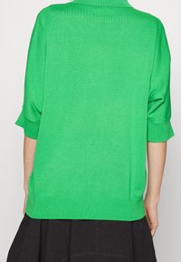 Maglione corto a maniche corte di colore verde, realizzato in maglia con una texture a costine e scollatura rotonda, con spacchi laterali e una vestibilità comoda.