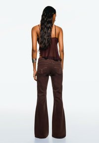 Brązowe dżinsy w kształcie dzwonów z widocznymi detalami szwów, połączone z ciemno-brązowym topem bez rękawów. Strój charakteryzuje się luźnym krojem i gładką teksturą.