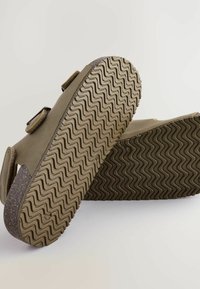 Brune slip-on sko med to justerbare stropper, teksturerede gummisåler og et zigzaggrebmønster for forbedret traction.
