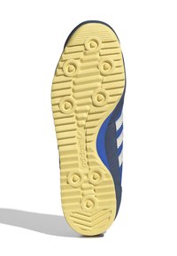 Shoe sole with a yellow rubber base, textured for grip. Features a blue upper with white stripes, rounded edges, and a classic athletic design.