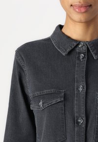 Dark gray denim shirt featuring a classic collar, button-up front, and two chest pockets with button closures. Soft texture and structured design.
