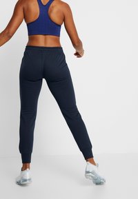 Námornické joggingové kalhoty s zúženým střihem a elastickým pasem, spárované s vzorovaným fialovým sportovním topem a průhlednými sportovními botami.