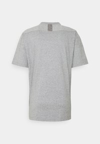 Šedé tričko s krátkým rukávem a kulatým výstřihem, vyrobené z měkké tkaniny, s texturovanou nášivkou na zadním výstřihu.