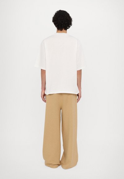 White oversized t-shirt with a round neckline paired with beige wide-leg pants. Soft cotton material, simple design, no visible patterns or accents.