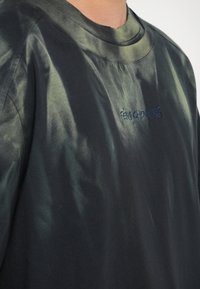 Tricou negru din bumbac, cu un model tie-dye în nuanțe de verde închis. Detalii notabile includ un decolteu rotund și un logo de marcă brodat.