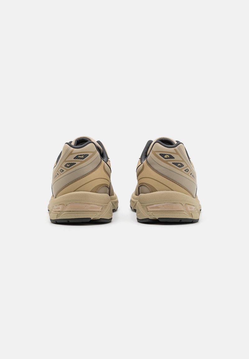 Une paire de chaussures de sport beiges et grises vues de l'arrière sur un fond blanc uni.