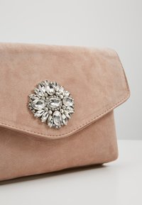 Pochette en daim rose avec une broche décorative en forme de fleur ornée de pierres acryliques transparentes et d'accents métalliques. Fermeture à rabat pliable.
