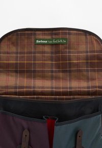 O interior da bolsa de tela colorida apresenta um padrão xadrez castanho e uma etiqueta verde. Inclui vários bolsos e acabamentos em couro.