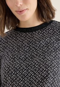 Top nero con un motivo testurizzato di righe verticali bianche e grigio chiaro, con un colletto nero glitterato. Tessuto morbido, design aderente.