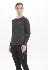 Langärmliges Sportoberteil aus dunkelgrauem Stoff mit Rundhalsausschnitt und dezentem Logo. Kombiniert mit schwarzen, enganliegenden Leggings mit weißen Akzenten.