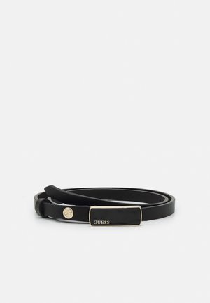 Ceinture fine en cuir noir avec boucle rectangulaire dorée portant l’étiquette "GUESS" et un petit détail bouton doré sur la sangle.