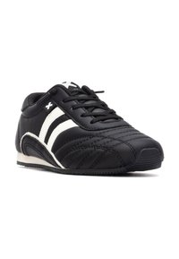 Zapatilla deportiva negra con rayas blancas, de material de cuero suave, punta redondeada, detalles cosidos y suela de goma texturizada.