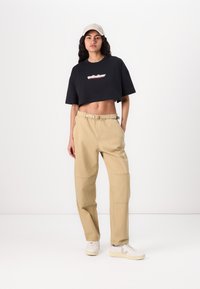 Maglietta nera crop con grafica "quiksilver", pantaloni cargo beige a vestibilità ampia e sneakers bianche con dettagli beige.
