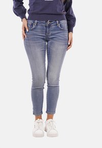 Jeans skinny blu in un lavaggio chiaro, con tasche frontali, chiusura a bottone e una classica texture in denim, abbinati a sneaker bianche.