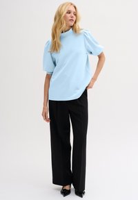 Top azzurro chiaro a maniche corte con un collo alto e maniche a sbuffo, abbinato a pantaloni neri a gamba larga e scarpe nere con punta.