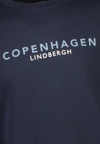Dunkelblaues Baumwoll-T-Shirt mit Rundhalsausschnitt, auf dem "KOPENHAGEN" in hellblau und "LINDBERGH" in weißer Schrift quer über die Brust gedruckt ist.