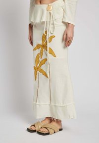 Cream-colored linen skirt featuring yellow palm tree embroidery, a frayed hem, and a drawstring waist tied with a wooden accent.