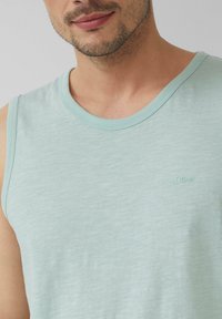 Helles blaues ärmelloses Tanktop aus weichem Stoff mit subtiler Textur. Verfügt über einen runden Ausschnitt und ein gesticktes Markennamensdetail.