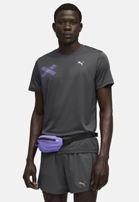 Graues Sport-T-Shirt mit lila Akzenten und Logo, kombiniert mit passenden Shorts und einer kleinen lila Bauchtasche mit einem schwarzen Riemen.