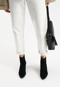 Białe wycięte spodnie z podwiniętymi nogawkami, w komplecie z czarnymi zamszowymi botkami za kostkę. Czarna torebka z frędzlami noszona jest po boku.