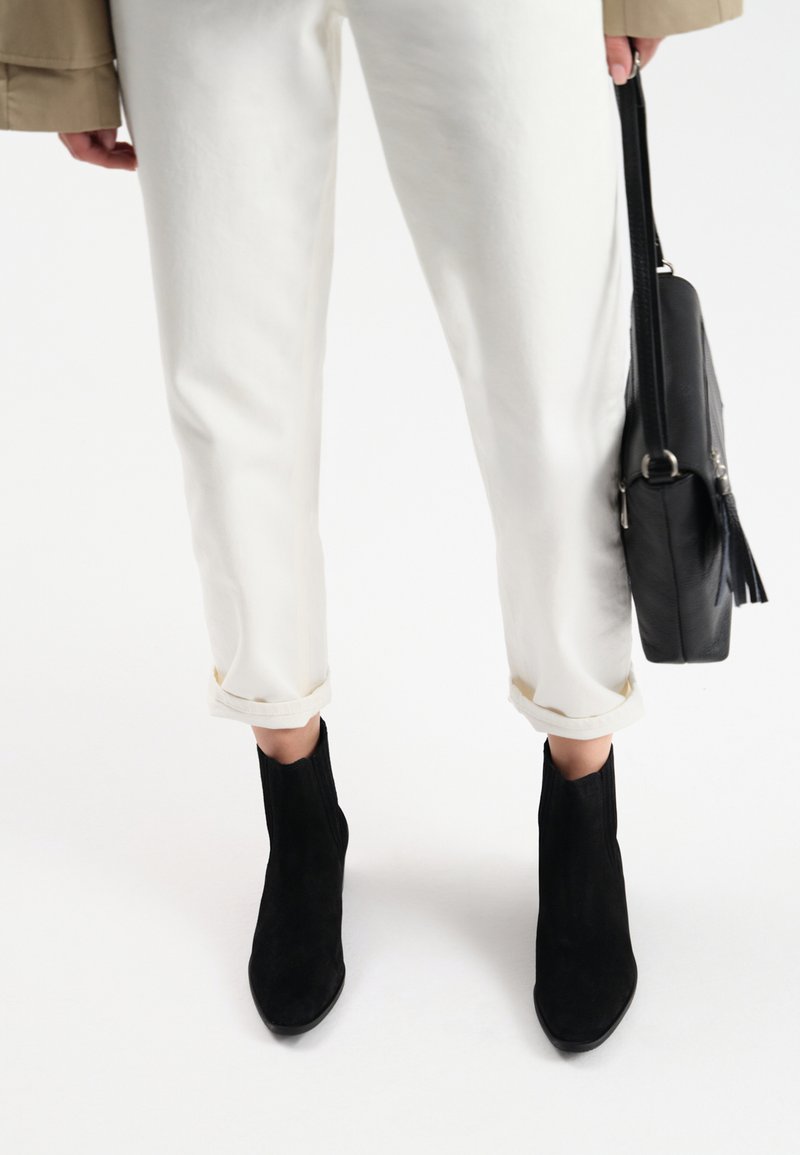 Białe wycięte spodnie z podwiniętymi nogawkami, w komplecie z czarnymi zamszowymi botkami za kostkę. Czarna torebka z frędzlami noszona jest po boku.