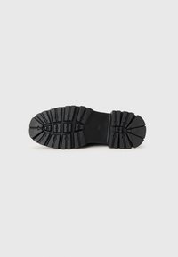 Suela de zapato de goma negra con surcos profundos y texturizados para agarre y durabilidad; puntera redondeada y ranuras con patrón para tracción.