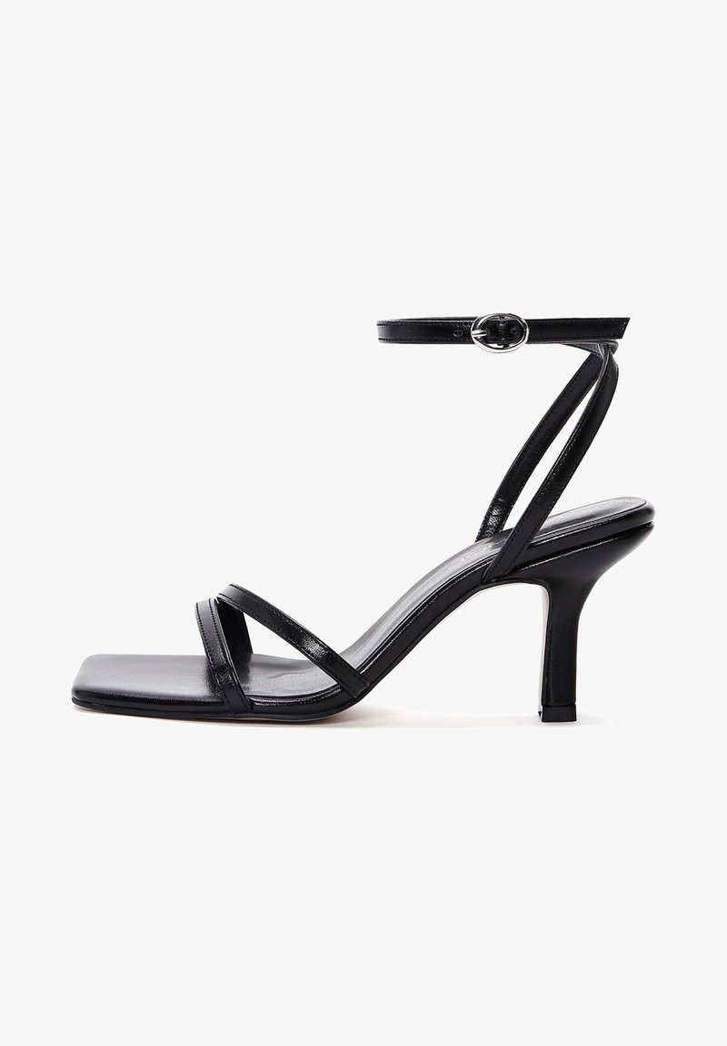 Sandale à talon haut noire pour femme avec bout carré, fines brides sur les orteils, une bride à la cheville avec boucle, et un talon moyen incurvé.