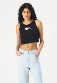 Top corto nero con logo rosso Quiksilver, abbinato a jeans a vita alta azzurri. Sfondo semplice con poche distrazioni.