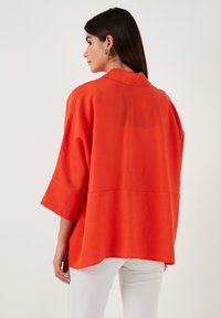 Bright orange oversized shirt with a collar, loose fit, three-quarter sleeves, and a straight hem, made of lightweight fabric.