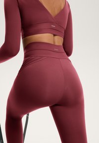 Bordeaux activewear set met een lange mouw top met wikkelontwerp en hoge taille leggings met textuuraccenten. Soepele stof.