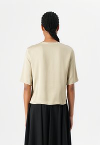 Kortermet beige topp laget av mykt materiale; har en avslappet passform og rund hals, presentert med et svart skjørt, minimalistisk design.