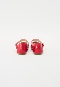 Bailarinas de cuero rojo con puntera redondeada, tacón pequeño y tira en el tobillo con hebilla. Textura suave y diseño sencillo.