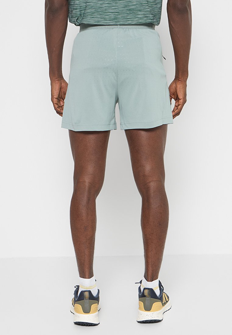 Shorts deportivos de color verde claro con una textura suave, cintura elástica y un corte relajado. Combinados con zapatillas deportivas blancas y marinas.