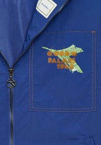 Giacca blu con chiusura a zip, fodera in rete e un design ricamato con "Palmes 1948" in arancione e verde sulla tasca del petto.