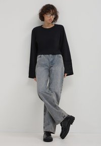 Maglione cropped nero con maniche a campana testurizzate, abbinato a jeans dritti azzurri e stivali alla caviglia neri chunky.