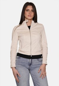 Giacca di pelle beige chiaro con design aderente, colletto alto e chiusura con zip. Presenta due tasche laterali e dettagli di cucitura discreti.