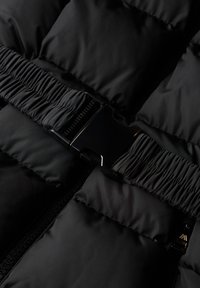 Close-up of black padded jacket with central black plastic buckle and elastic cinched belt detail.