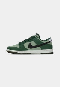 Nike Dunk Low sneaker, amely sötétzöld és világoszöld velúr keverékéből készült, fekete Swoosh logóval, fehér középtalppal és texturált gumitalppal.