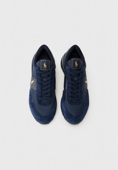 Des baskets bleu marine en matière mixte de daim et de mesh, avec un design lacé et un accent de logo doré sur la languette et le panneau latéral.