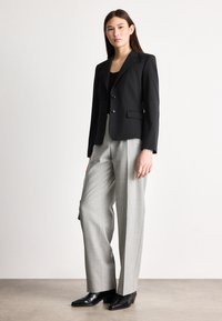 Mustast kohandatud jakk kahte nööpi, hallid kõrge vöökohaga püksid ja teravate kontsadega mustad kingad. Sile kangas ja struktureeritud disain.