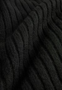 Schwarzer Strickstoff mit einem strukturierten, gerippten Design und hervorstehenden sowie vertieften Mustern. Weiche und flauschige Textur mit sichtbaren Fasern.