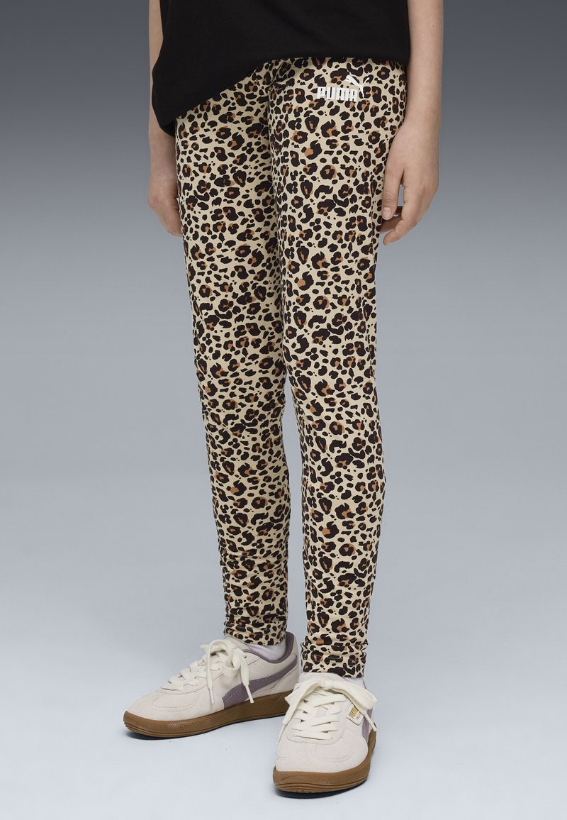 Leggings con stampa leopardata in beige con macchie nere e marroni. Design aderente e materiale elastico. Abbinati a scarpe da ginnastica bianche e grigie.