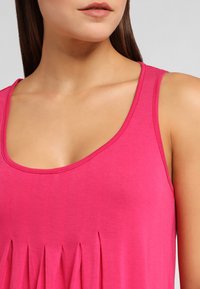 Pink sleeveless top featuring a scoop neckline and pleated detail along the front, made from a smooth fabric with a soft texture.