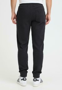 Czarne spodnie dresowe wykonane z teksturowanej tkaniny, z tylną kieszenią i elastycznym paskiem w talii, w zestawieniu z białymi sneakersami z czarnymi akcentami.