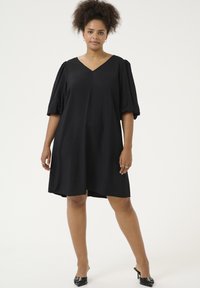 Robe noire à manches courtes avec un décolleté en V, coupe ample et longueur au genou. Texture de tissu lisse, design minimaliste sans motifs ni embellissements.