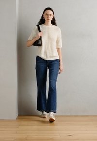 Maglione bianco a maglia testurizzata con maniche corte, abbinato a jeans a zampa d'elefante blu scuro e sneakers bianche; porta una borsa nera.