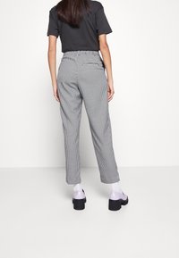 Black and white checkered trousers with a relaxed fit, featuring an elastic waistband and tapered legs. Complemented by purple footwear.