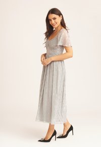 Grey mid-length dress with short flutter sleeves and gathered bodice, featuring a shimmering pattern. Paired with black heels with embellishments.